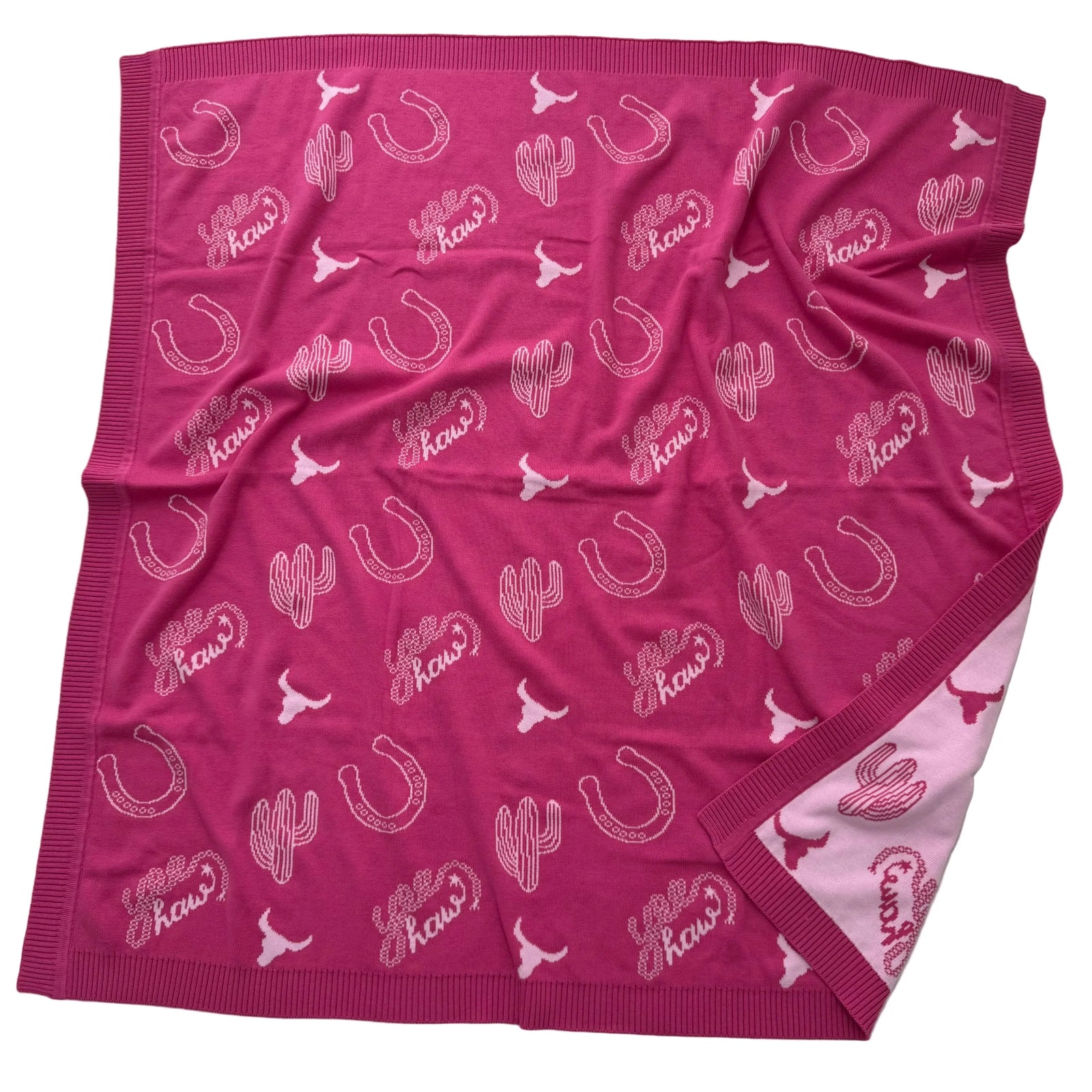 A pink fleece throw blanket featuring a repeating pattern of white horseshoes, cacti, longhorns, and the word 'Kows' in stylized script. The blanket is laid flat on a white background, showing its ribbed knit borders and a lighter pink reverse side.