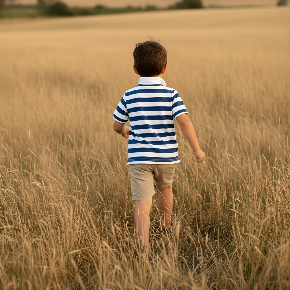 Child in a striped shirt walking through a field of tall grass with rolling hills in the background
