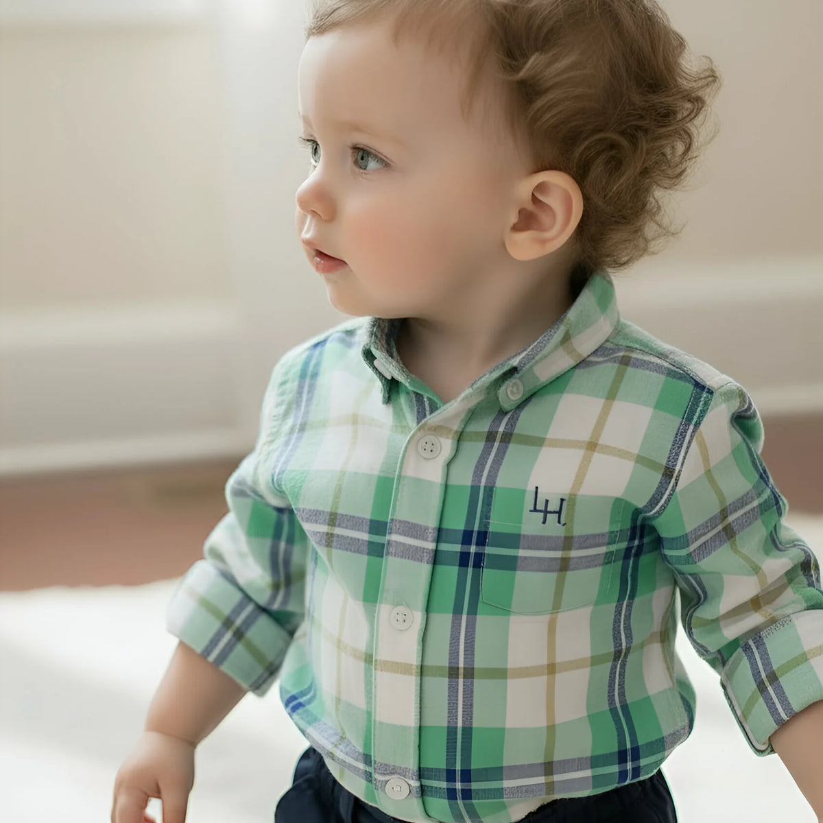 Child wearing a green plaid shirt with a logo on a neutral background