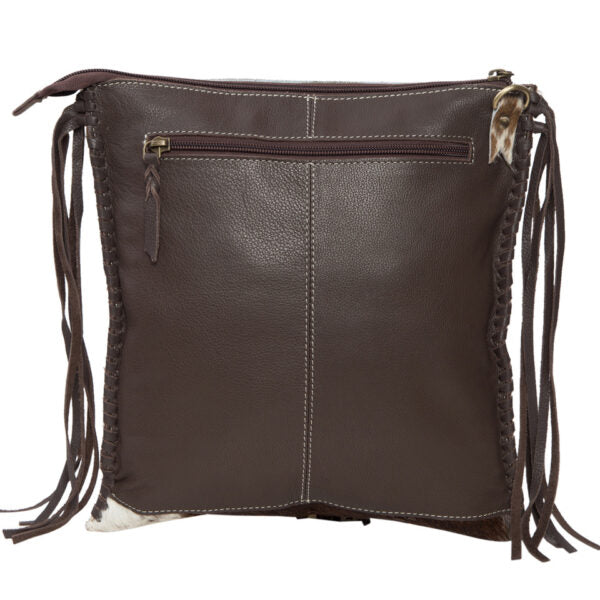 Chillan Tooling Leather Cowhide Sling Bag with Playing Cards Paint Highlight. A woman holding a bag with a cowhide pattern in a sunny outdoor setting.