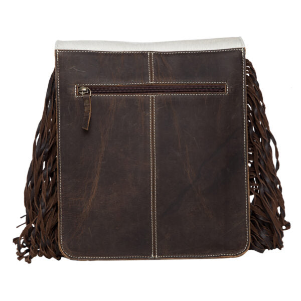 Women's Tooling Leather Flap Sling Cowhide Bag With Fringes. Woman holding a brown handbag with white floral design on a cobblestone street.
