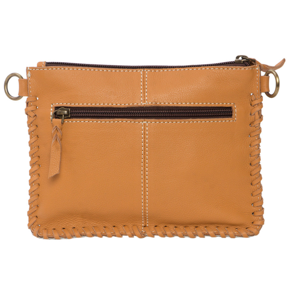 Volcan Tan Tooling Leather Cowhide Small Clutch Bag. Woman holding a cowhide-patterned handbag outdoors with greenery in the background