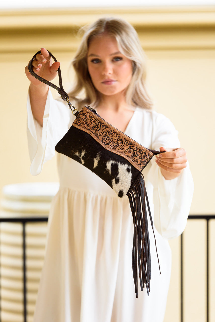 Salvador Tooling Leather Tassel Clutch. Woman holding a decorative belt with fringe against a neutral background