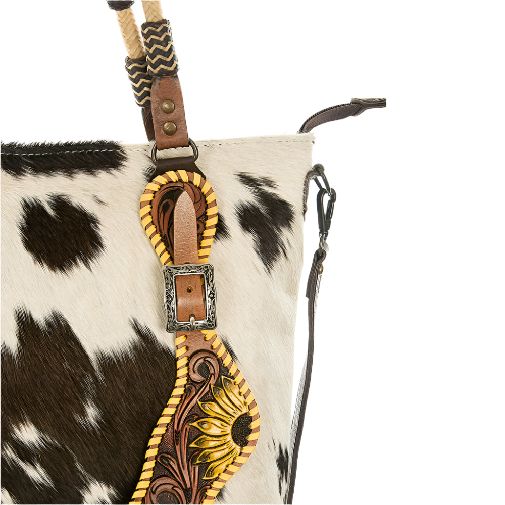 Close-up of a cowhide bag with decorative leather strap and sunflower design.