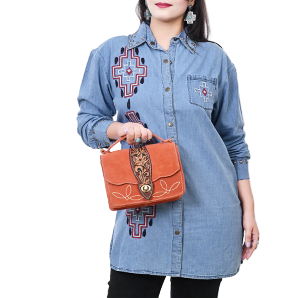 American Darling Burnt Orange Suede Western Shoulder Bag. Woman wearing a blue embroidered shirt holding an orange handbag with intricate designs.