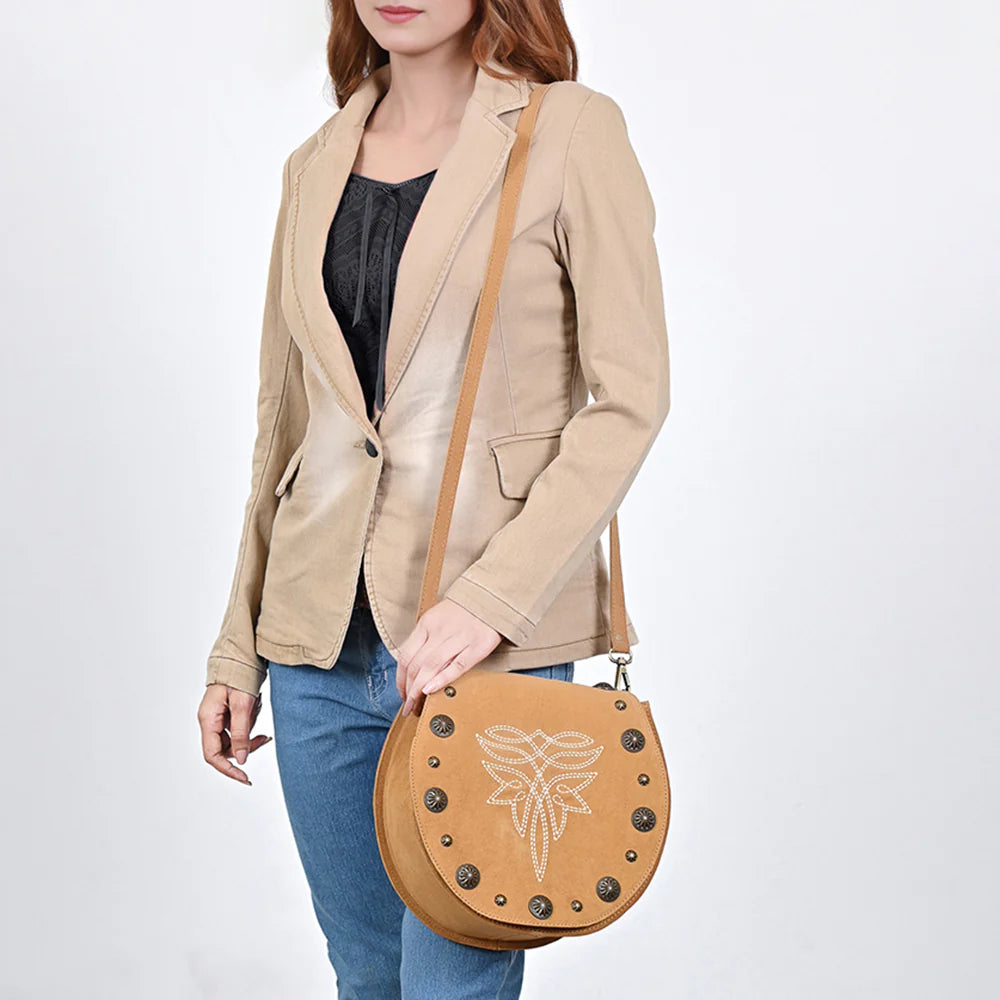 American Darling Suede Boot Stitch Western Handbag. Woman holding a tan leather handbag with decorative elements on a white background