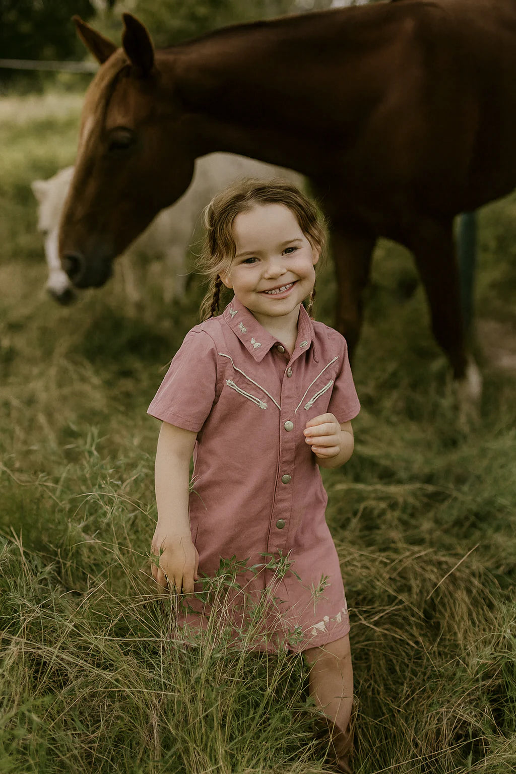 Little Windmill Girl's Arizona Western Blush Pink Dress. Young girl in a pink dress standing in a field with a horse in the background