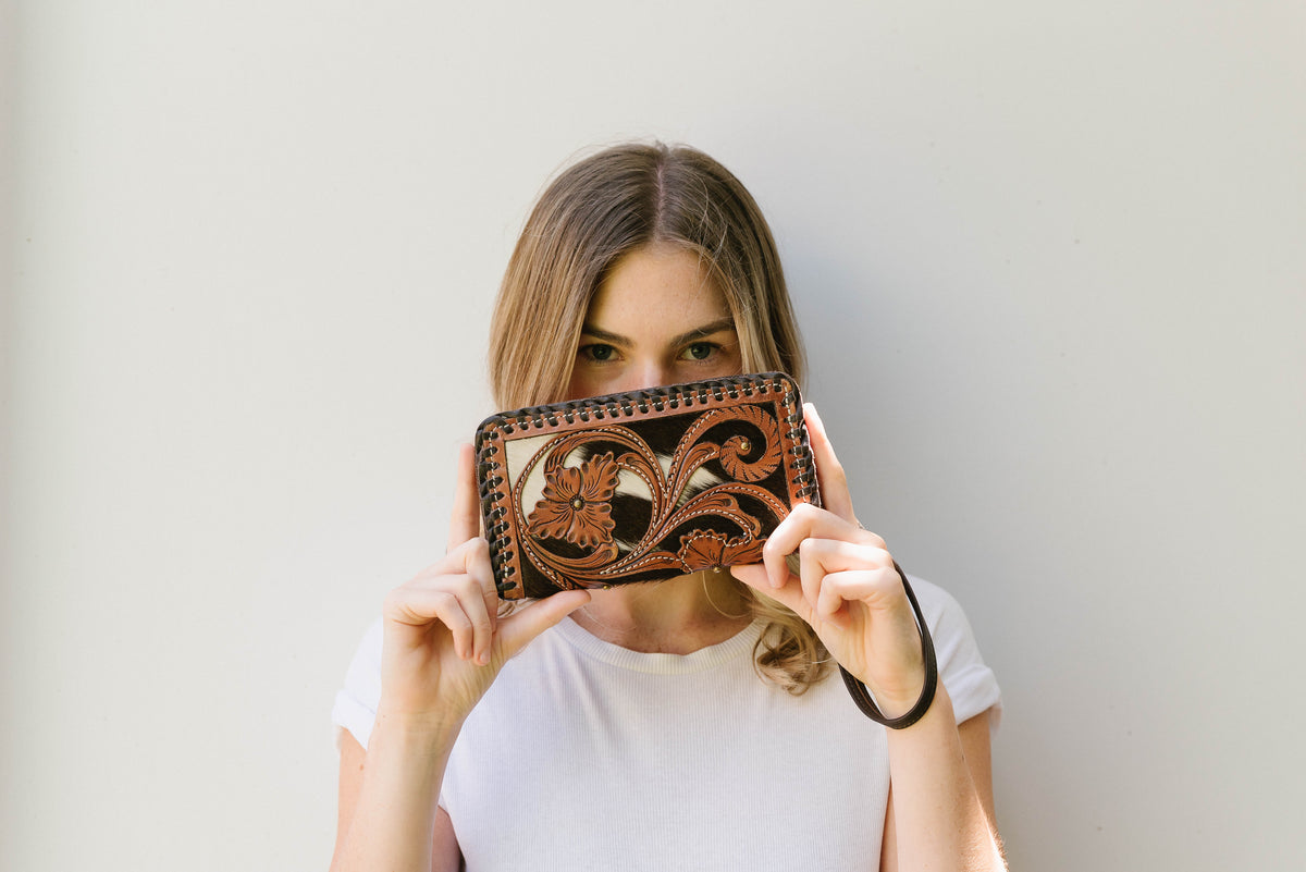 Woman holding a decorative brown leather wallet in front of her face against a plain background