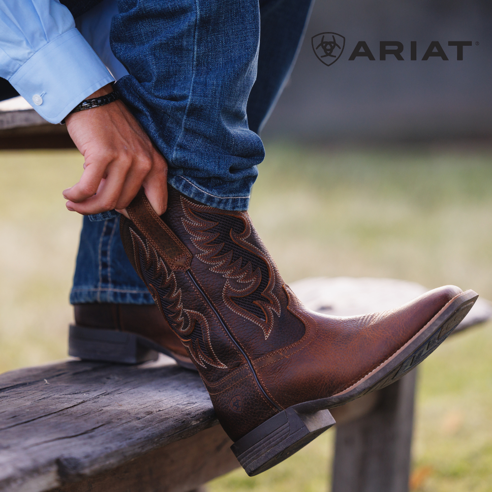 Brown cowboy boot with intricate stitching on a wooden bench, Ariat logo visible