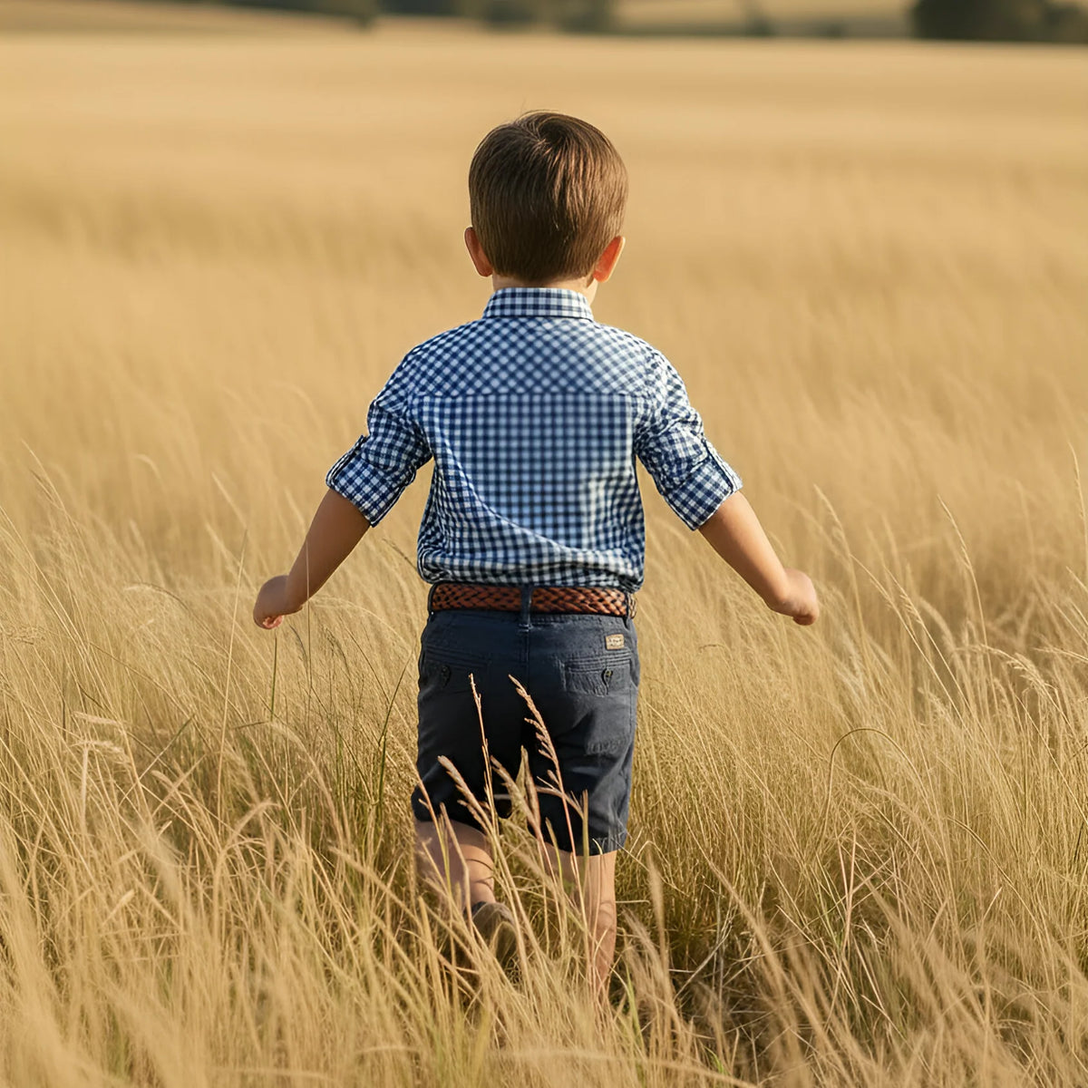 Child in a blue checkered shirt walking through tall golden grass.