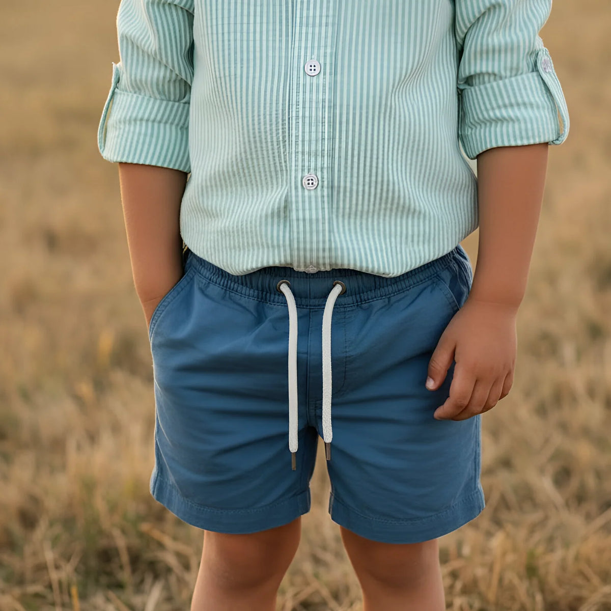 Person wearing a light green striped shirt and blue shorts standing in a field.