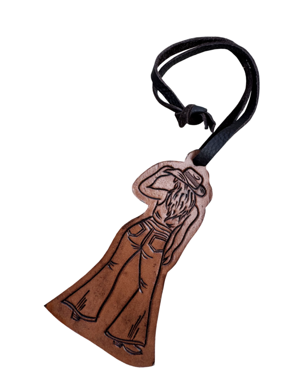 A brown leather pendant shaped like a cowboy in a long coat and hat, attached to a black leather loop, shown on a plain white background.