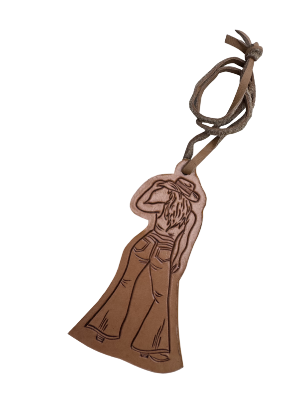 A brown leather luggage tag featuring an engraved cowboy silhouette wearing a hat and jeans, attached to a matching brown leather looped strap, shown on a plain white background.