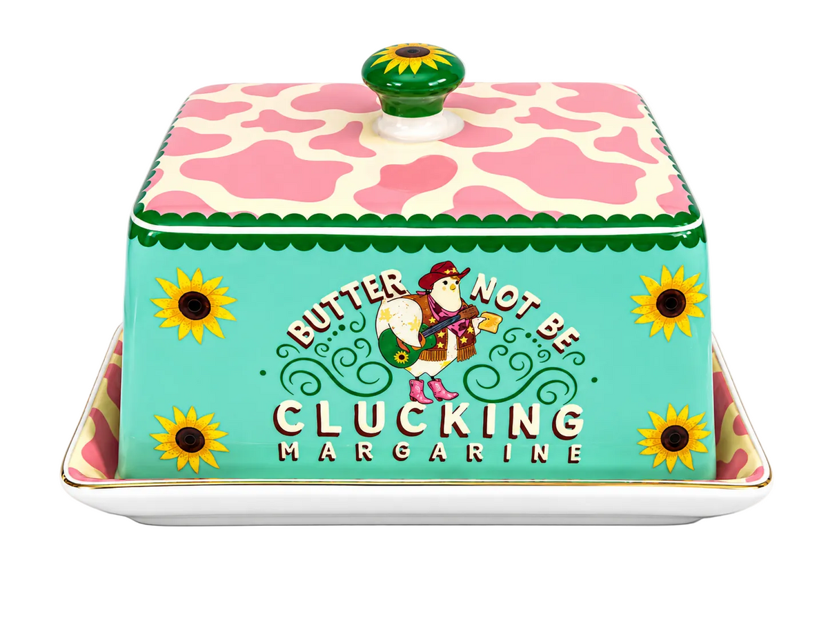 A decorative ceramic butter dish with a lid, featuring a turquoise front panel with the text 'BUTTER NOT BE CLUCKING MARGARINE' and a cartoon duck character, topped with a pink and cream cow-print lid and a green sunflower knob, shown on a white background.