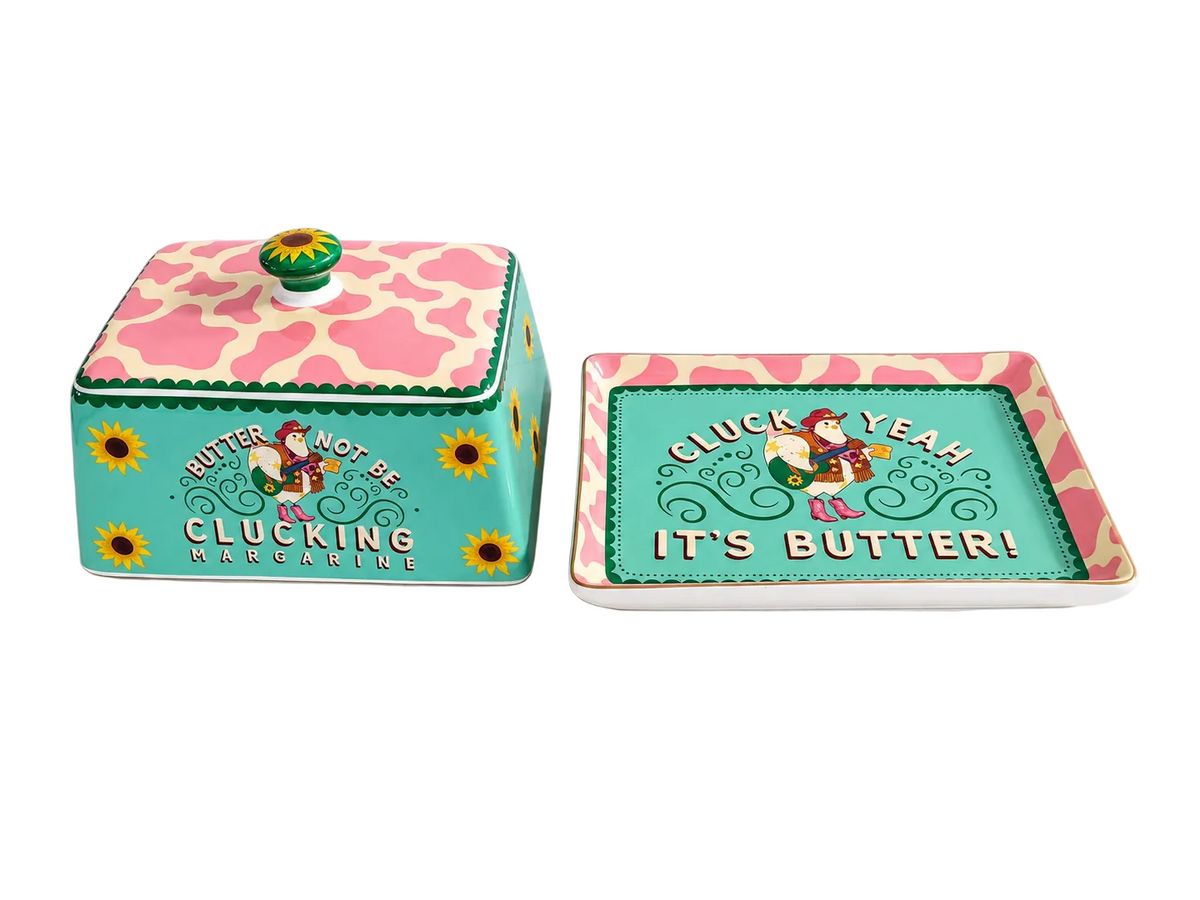 A matching butter dish and tray set with a humorous cartoon design. The rectangular lidded butter dish on the left has a turquoise body, pink and beige giraffe-patterned lid, and a green and yellow knob.
