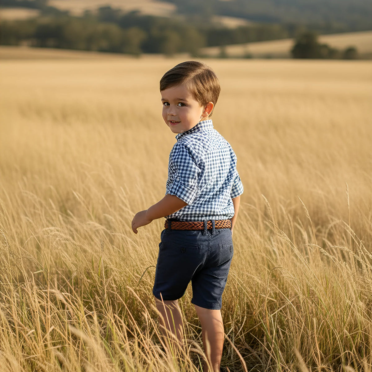 Young boy standing in a field of tall golden grass with a clear sky.