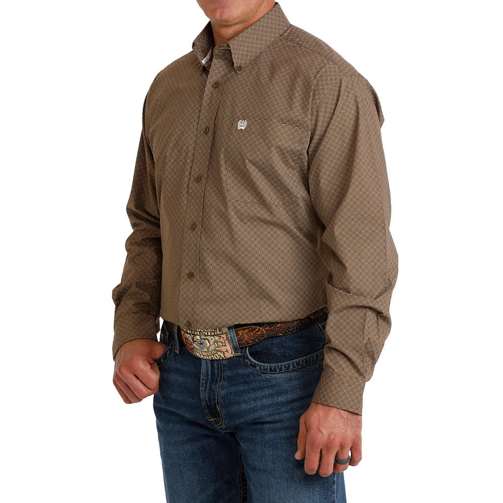 A man wearing a brown long-sleeve western shirt with a subtle geometric pattern, tucked into blue jeans with a western belt.