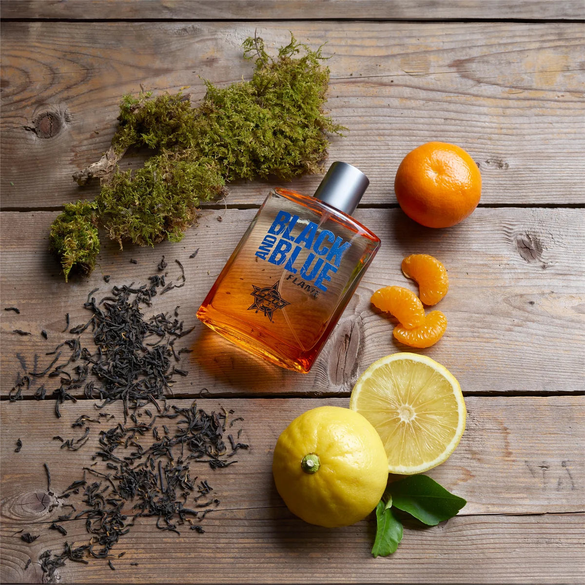 Orange bottle labeled 'Black and Blue' with lemons, oranges, and tea leaves on a wooden surface