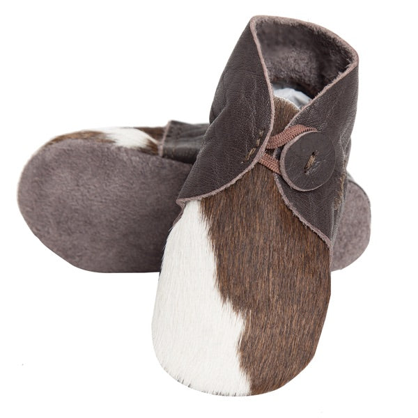 A pair of baby moccasins made from brown and white cowhide with dark brown faux-leather trim and a decorative button, shown on a plain white background.