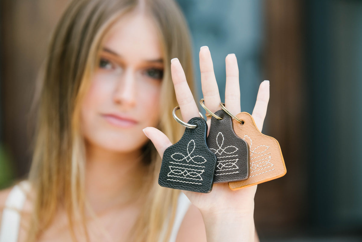 Woman holding two leather keychains with floral designs.