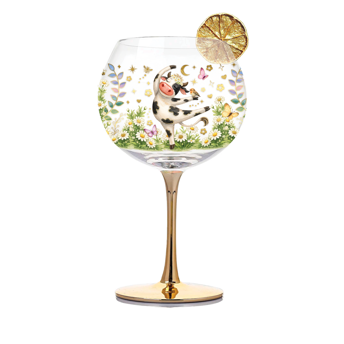 A clear stemmed wine glass with a gold-toned base and stem, decorated with a whimsical garden scene featuring a black-and-white cow, flowers, butterflies, and gold hearts. A lemon slice garnish rests on the rim.