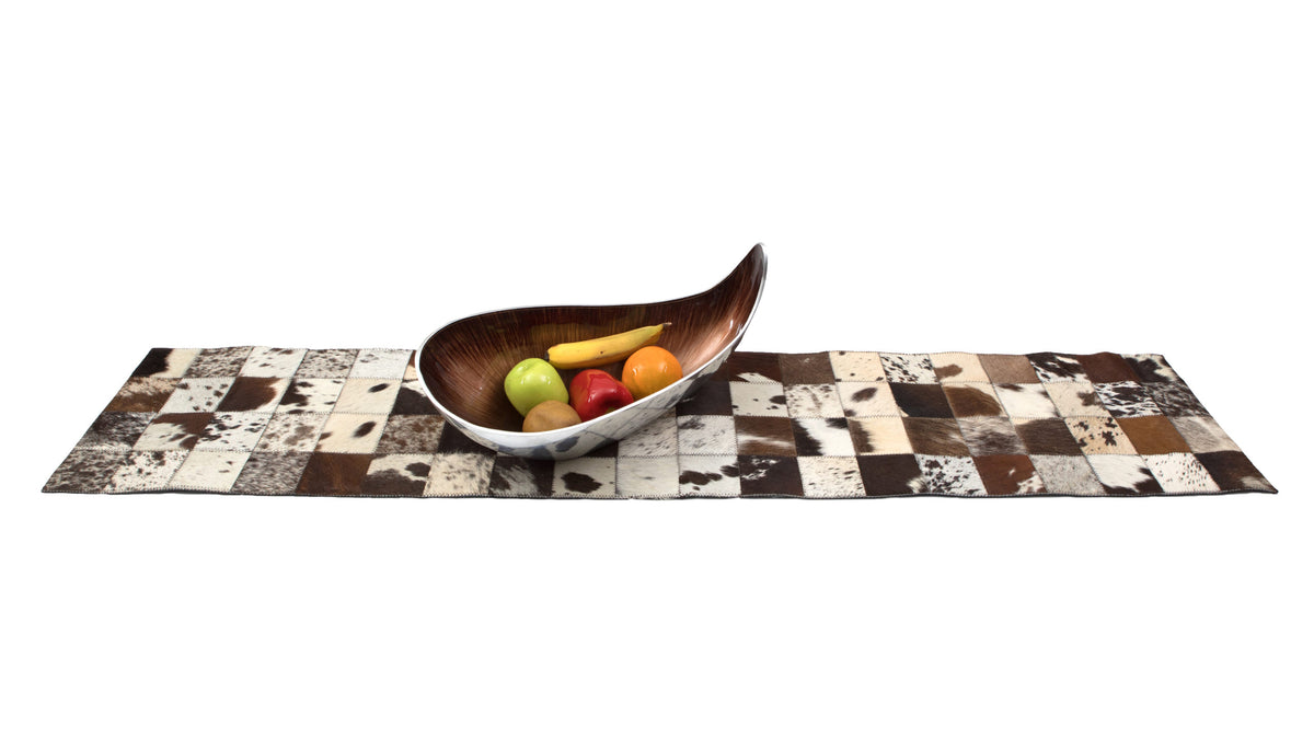 Cowhide Table Runner. Decorative cowhide rug with a wooden bowl containing fruits on a white background