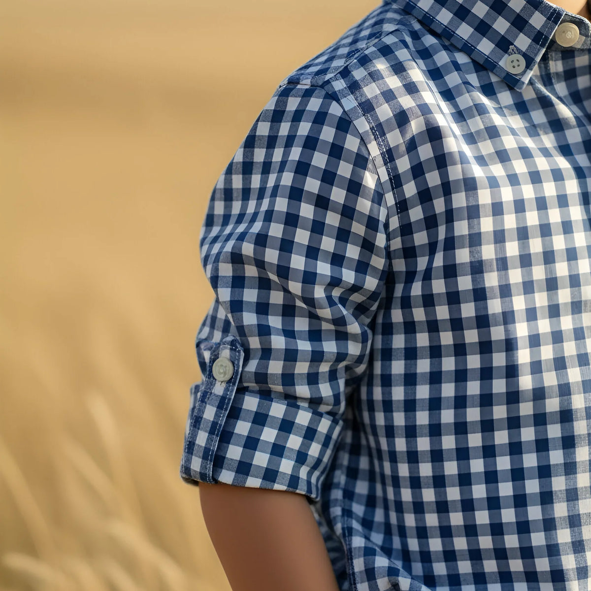 Person wearing a blue and white checkered shirt with rolled-up sleeves against a beige background