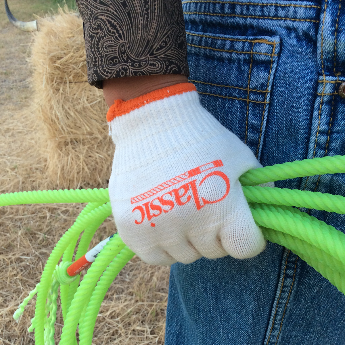Classic Deluxe Children's Roping Glove 12 Pack. A child's hand wearing a white and orange Classic brand rope glove, holding onto a green rope.