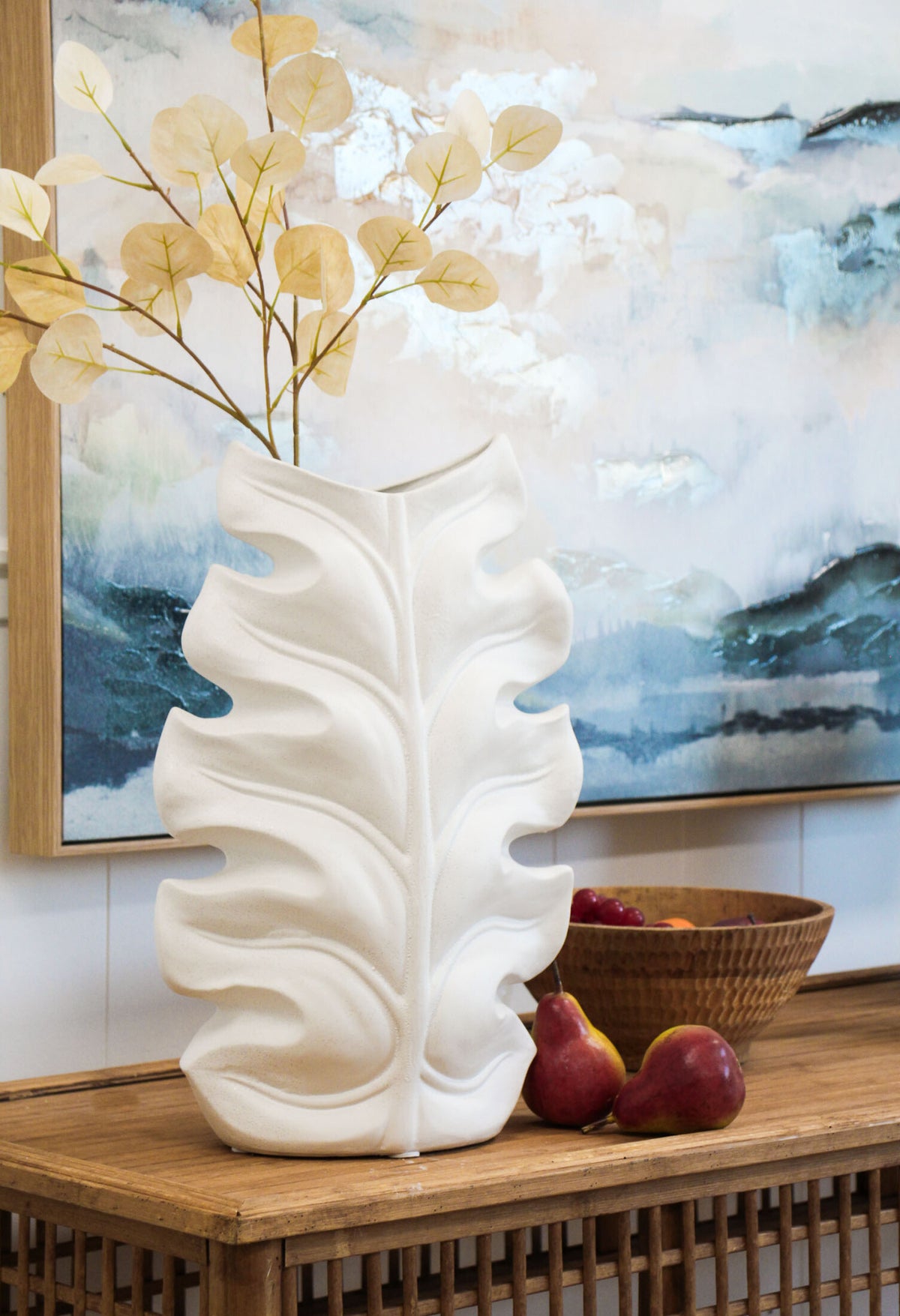 Rustic White Leaf Vase. White decorative vase on a wooden surface with a painting in the background