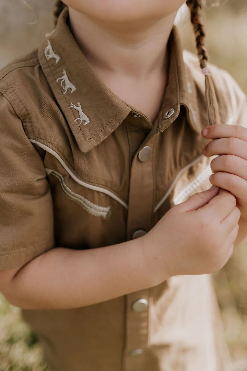 Little Windmill Cheyenne Western Mocha Dress. Child wearing a brown shirt with embroidered details in an outdoor setting