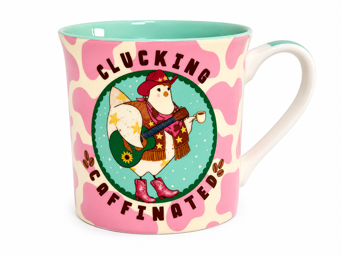 A ceramic coffee mug with a pink and cream cow print pattern, featuring a central illustration of a penguin wearing a cowboy hat and boots, with the text 'CLUCKING CAFFINATED' on a white background.