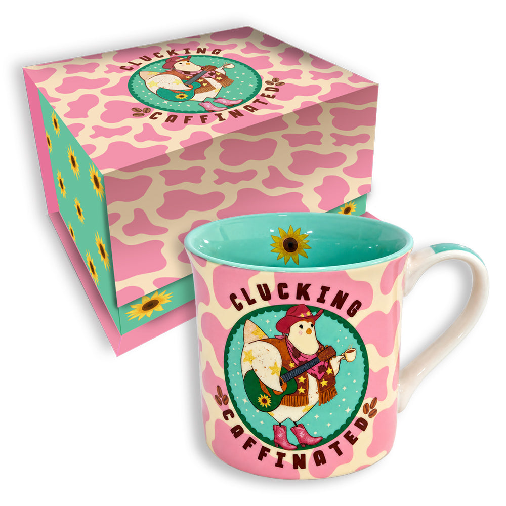 A pink and cream cow-print ceramic mug with a turquoise interior and handle, featuring a cartoon rabbit in a hat and the text 'CLUCKING COFFINATE!', shown in front of its matching patterned gift box.