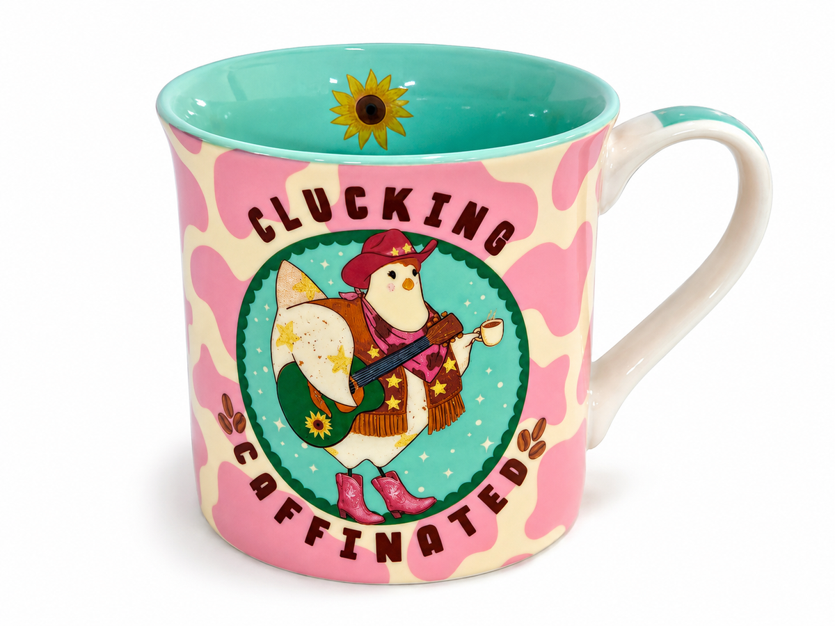 A ceramic coffee mug with a pink and cream cow print pattern, featuring a cartoon chicken playing guitar inside a green circle with the text 'CLUCKING CAFFINATED'. The inside of the mug is turquoise, and the handle is white.