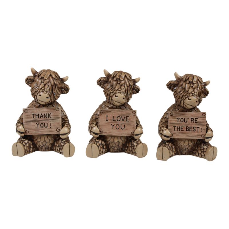 Three decorative Highland cow figurines with wooden signs on a white background