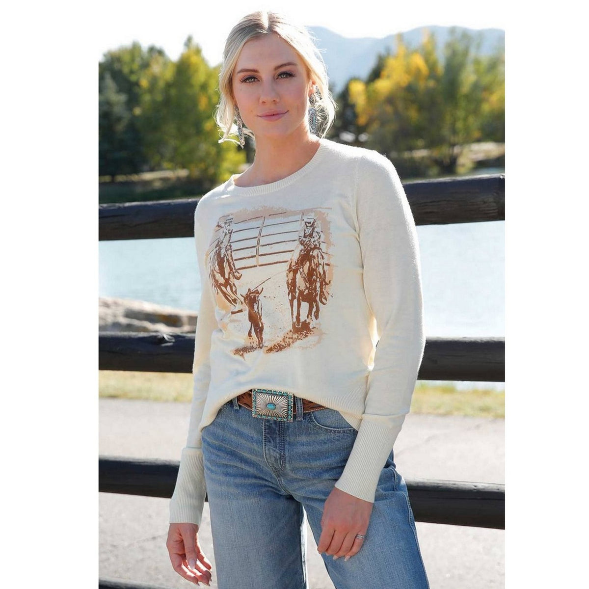 Cruel Denim Women&#39;s Roper Graphic Lightweight Sweater. Woman wearing a cream sweater with horse print outdoors