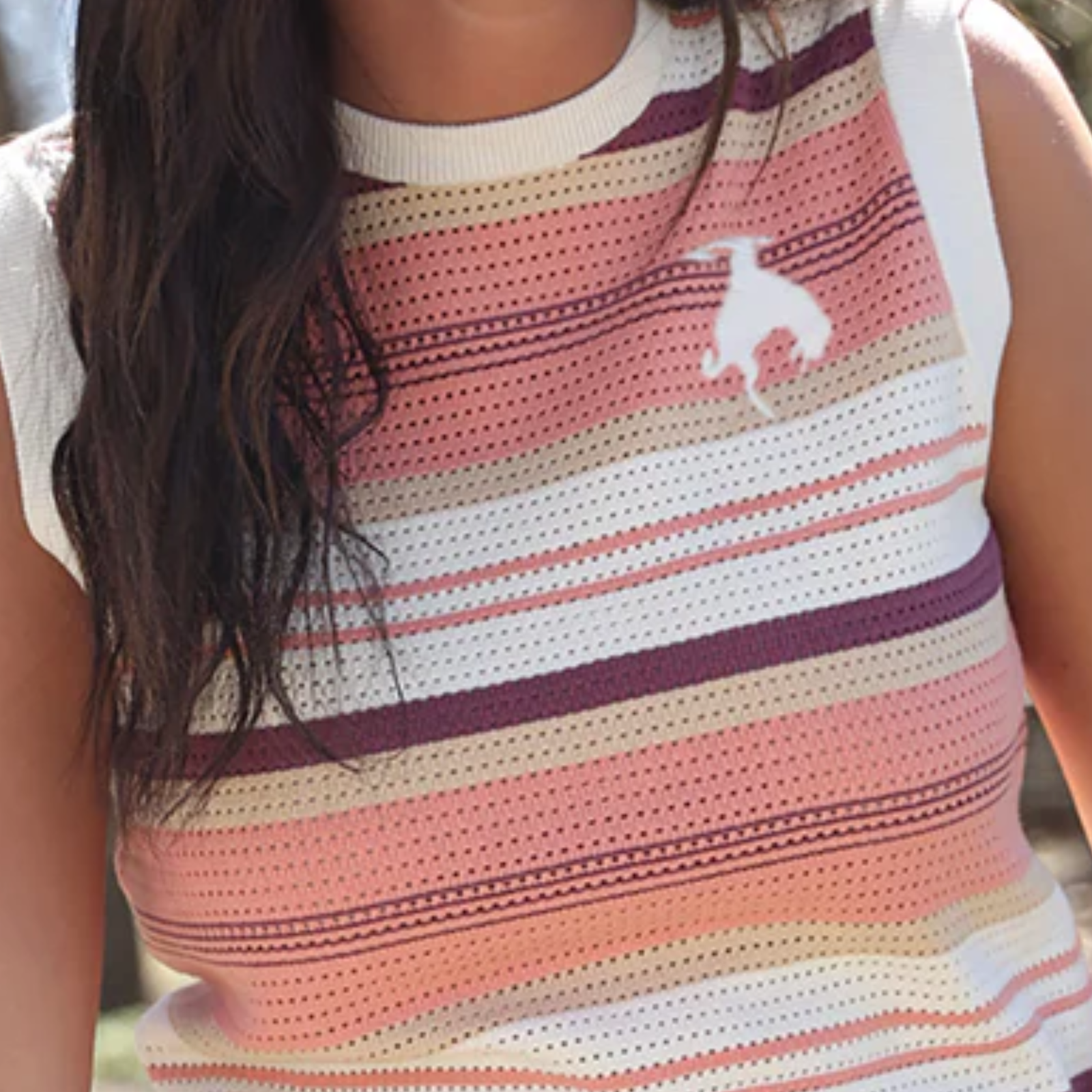 Person wearing a striped sleeveless top with a logo, outdoors.