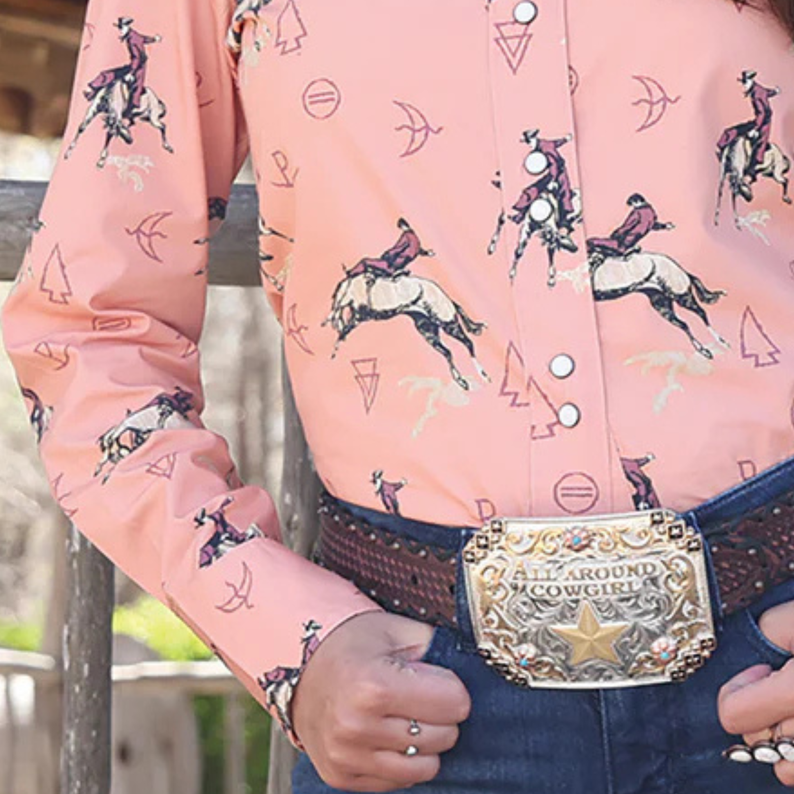 Person wearing a pink shirt with horse and rider pattern, holding a cowboy hat.