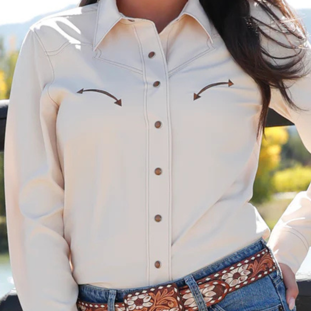 Beige button-up shirt with brown accents worn by a person, with a blurred outdoor background.