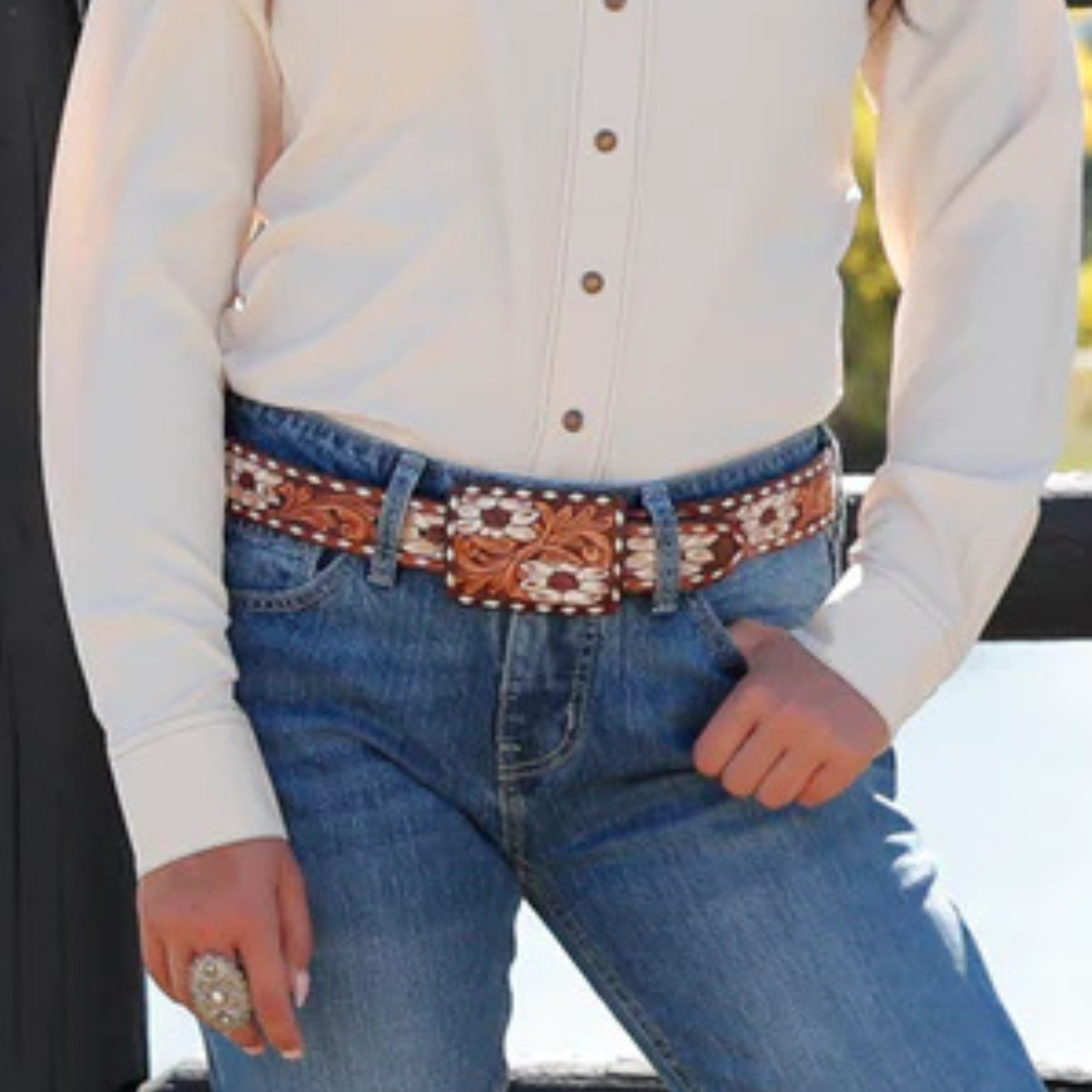 Person wearing blue jeans with a decorative belt and a white shirt.