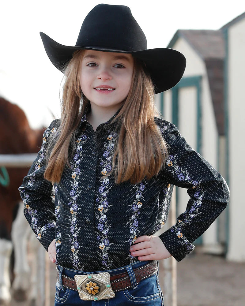 Child wearing a black cowboy hat and patterned shirt with a horse in the background