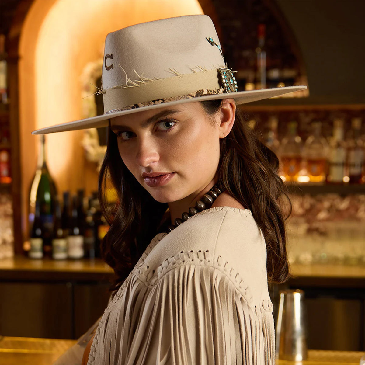 Charlie One Horse Spear Point Felt Cowboy Hat. Woman wearing a beige hat and fringe top in a bar setting with bottles in the background