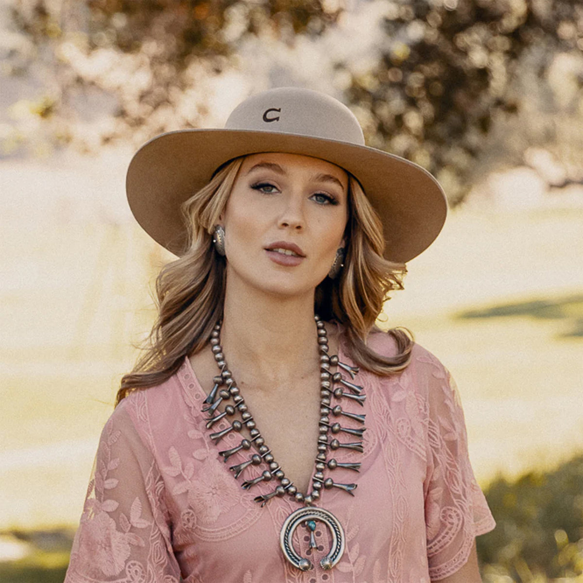 Charlie 1 Horse Wanderlust Felt Cowboy Hat. A beige wool cowboy hat with a bubble crown and a brim, featuring a woven hatband with a silver side concho and a feather, and the Charlie 1 Horse brand logo on the crown.