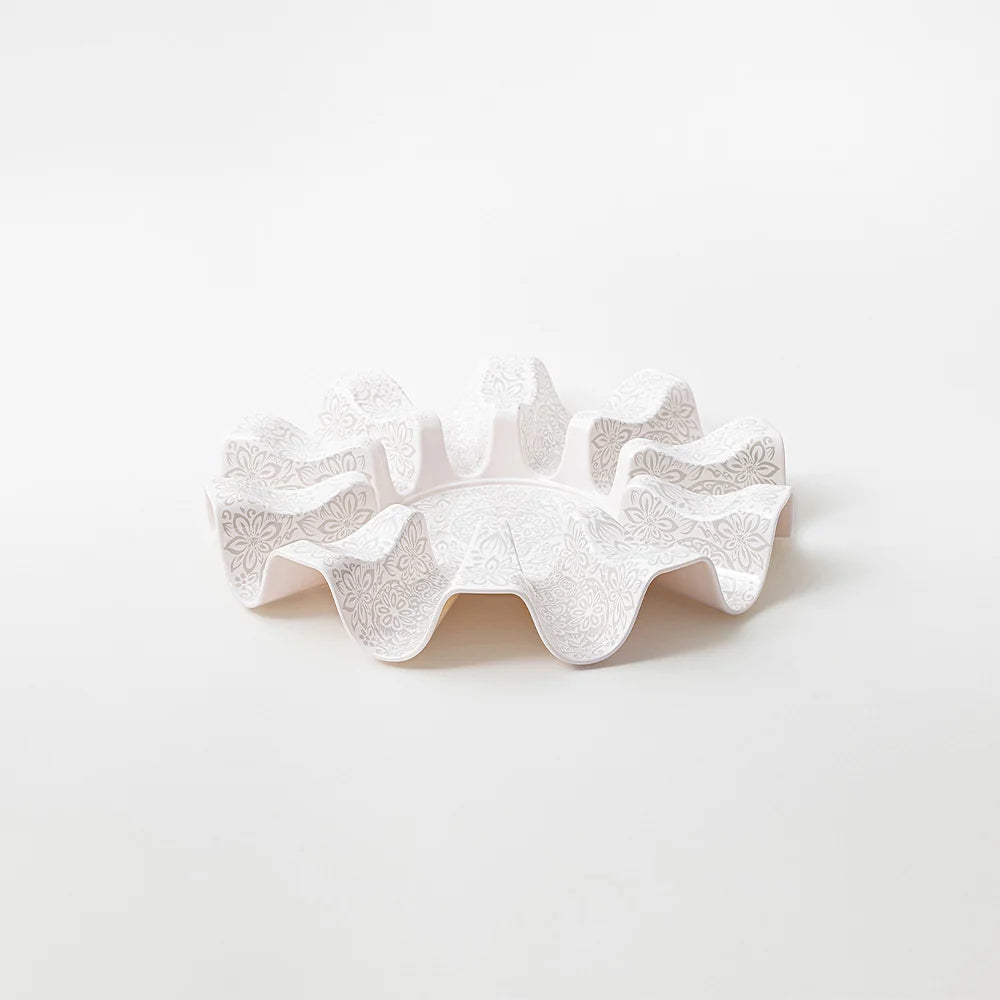 A white ceramic ruffled dish with embossed floral patterns, photographed on a seamless white background.