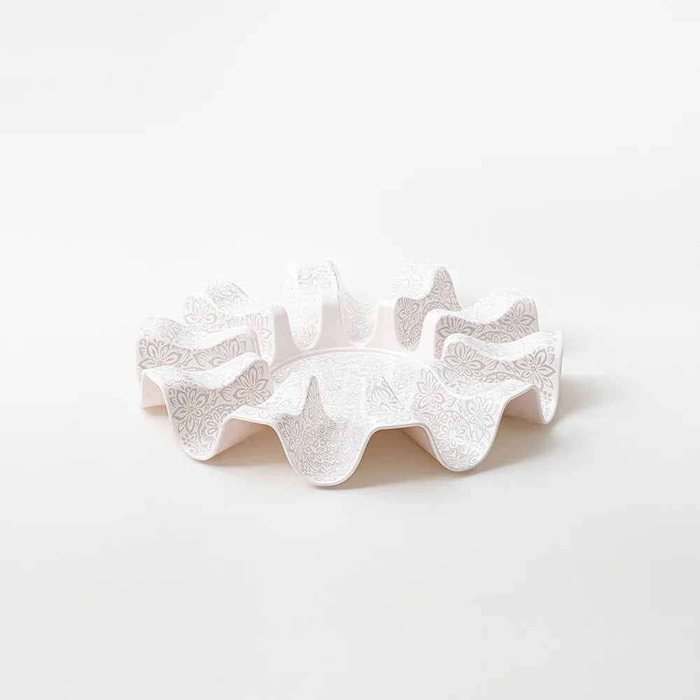 A white ceramic ruffled dish with embossed floral patterns, photographed on a seamless white background.