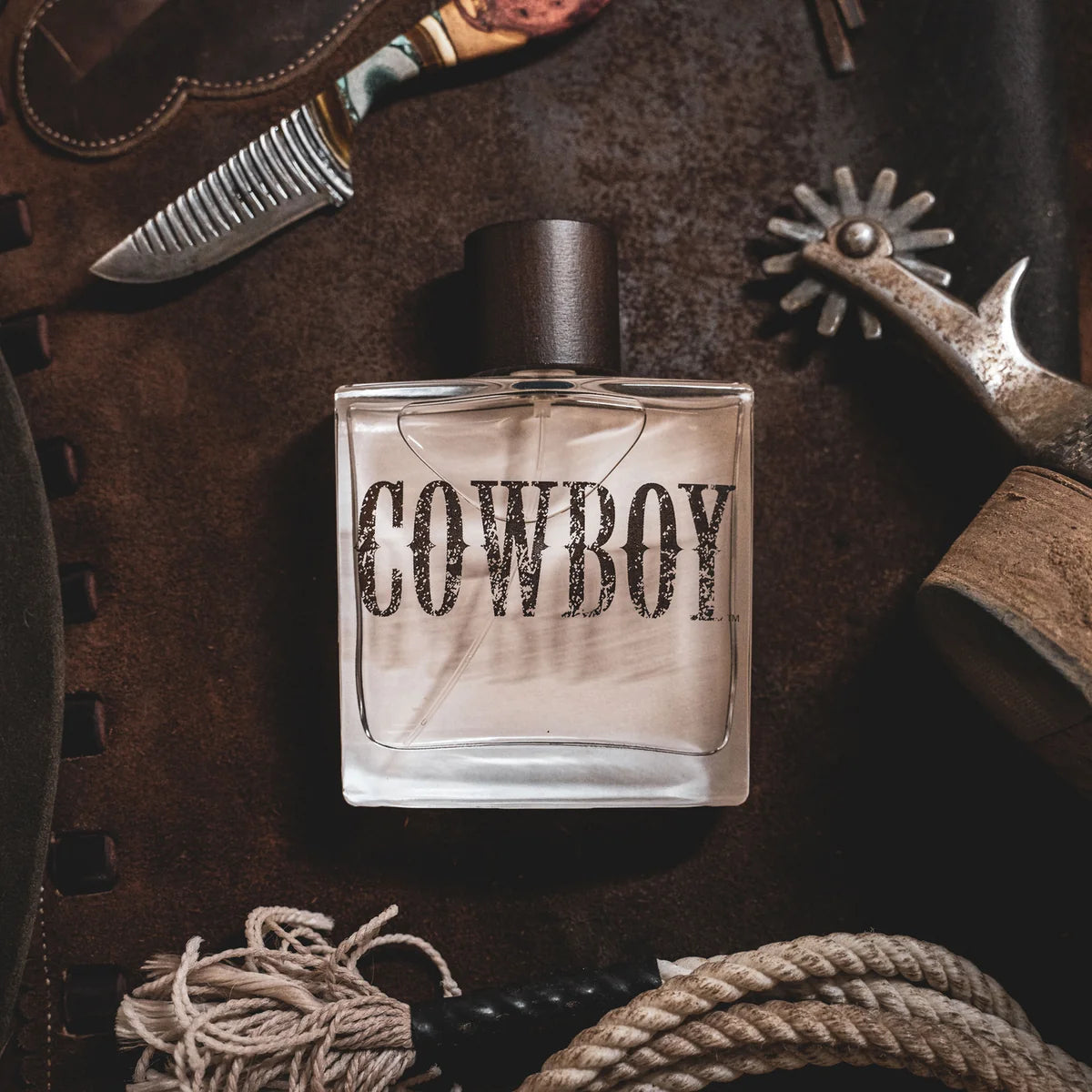 Perfume bottle labeled 'Cowboy' surrounded by cowboy-themed items on a textured surface