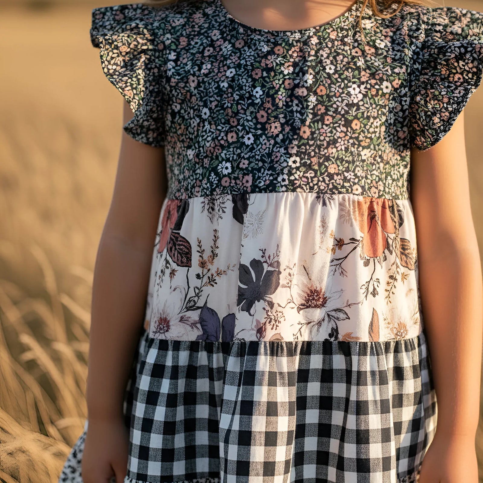 Young girl in a patterned dress standing in a field with a sunset background