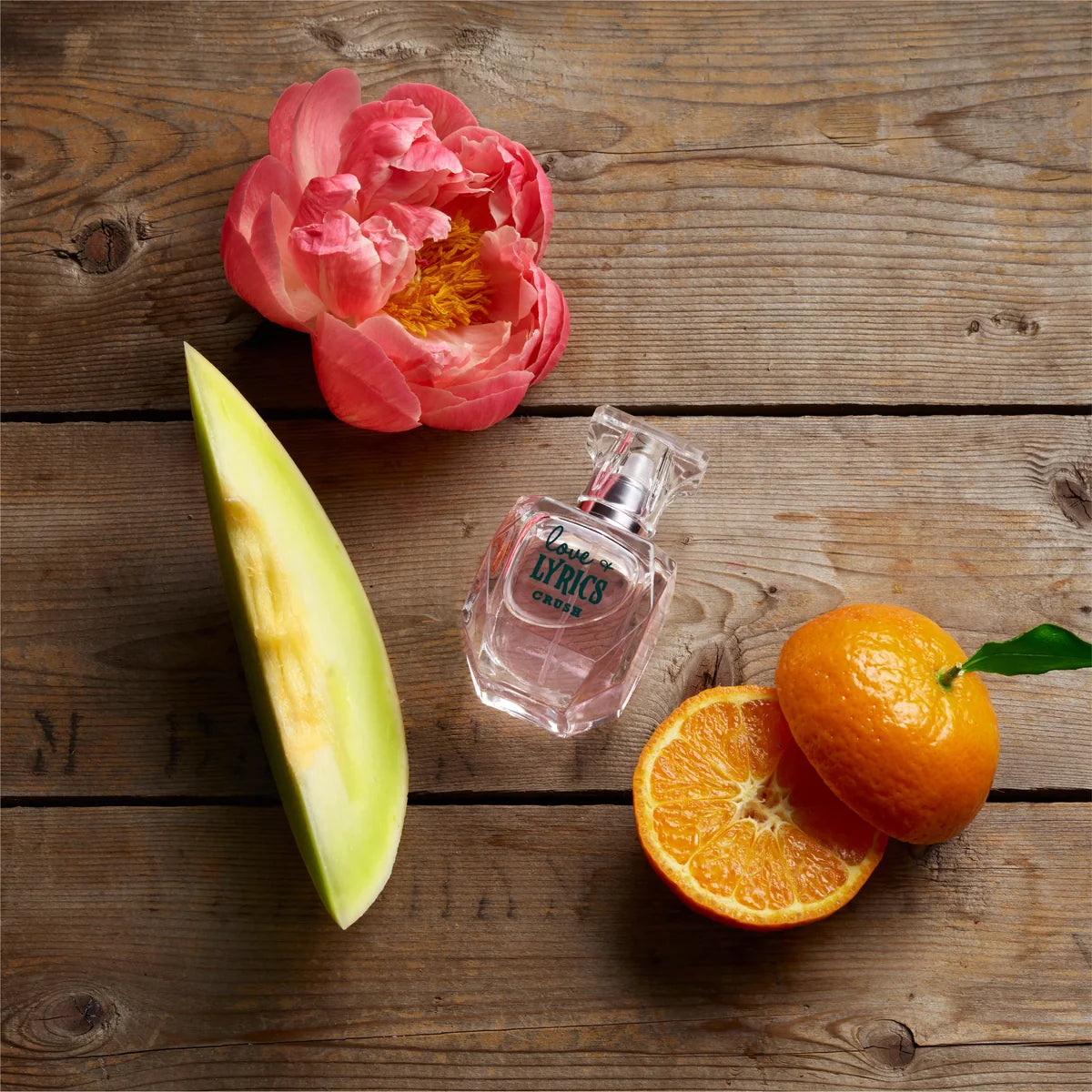 Perfume bottle with a pink flower and sliced fruits on a wooden surface