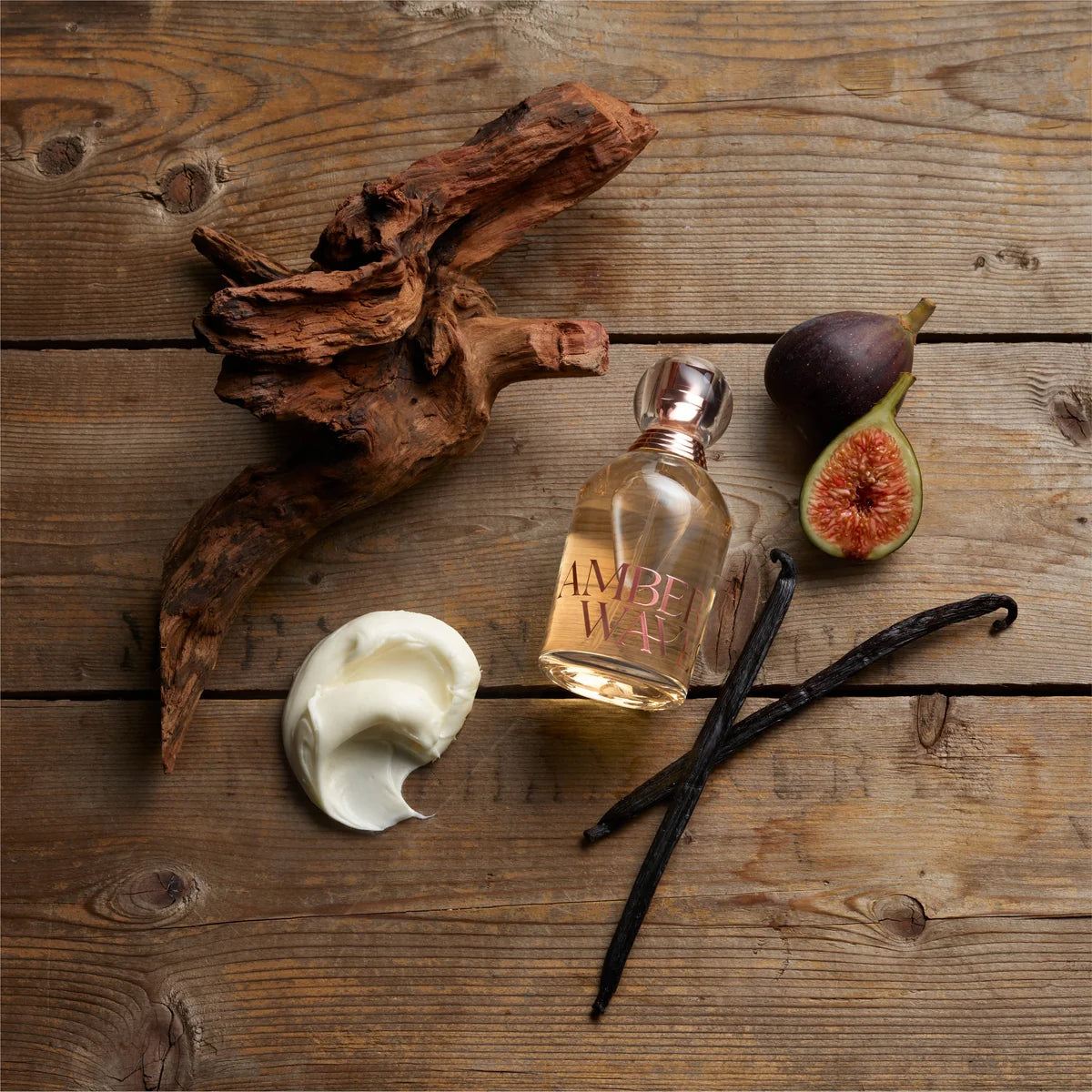 Amber Wax perfume bottle with vanilla beans, figs, and cream on a wooden surface