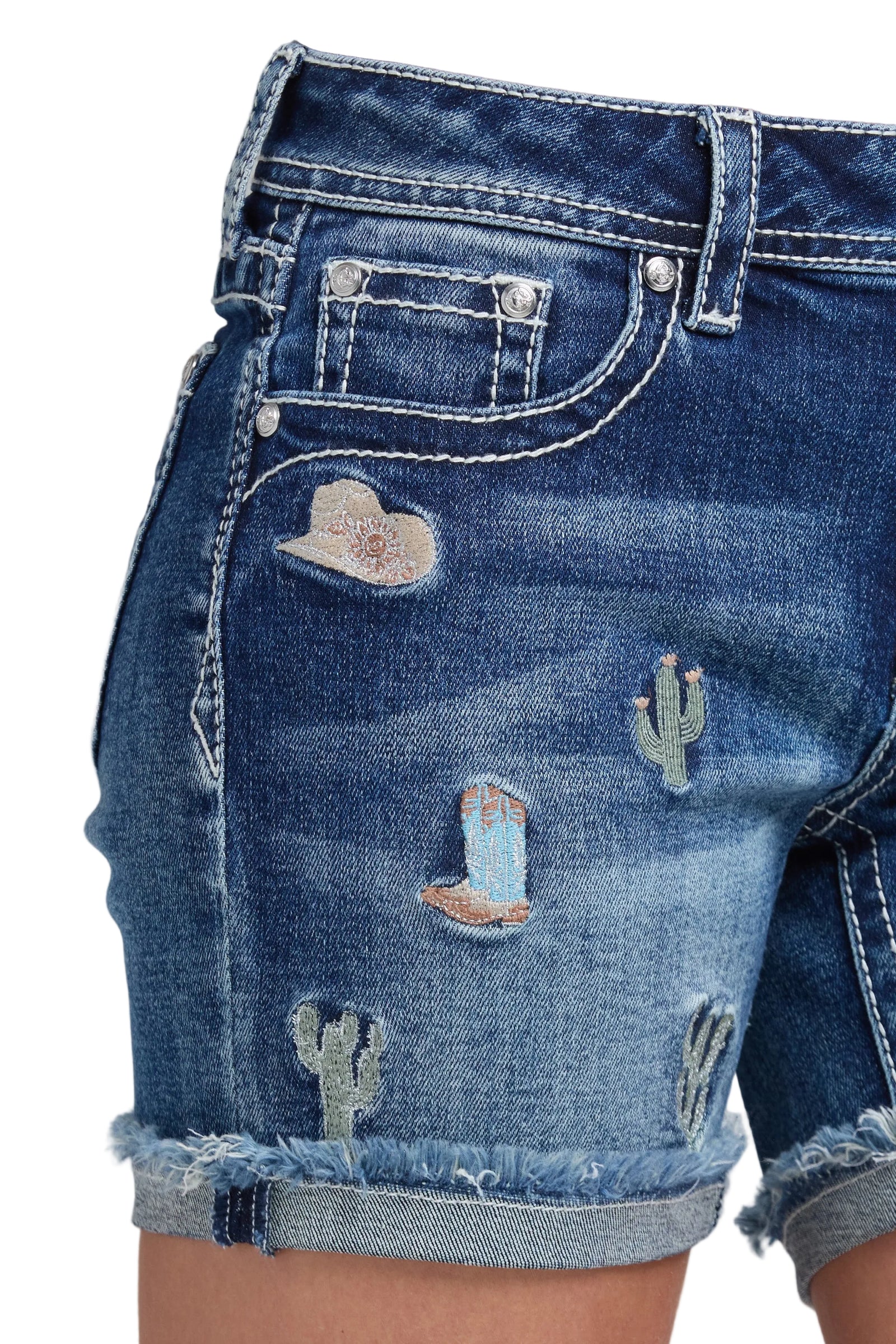 Person wearing distressed denim shorts and brown cowboy boots on a gray background