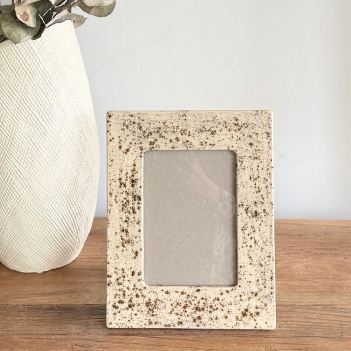 Speckled stone picture frame on a wooden surface with a white vase in the background